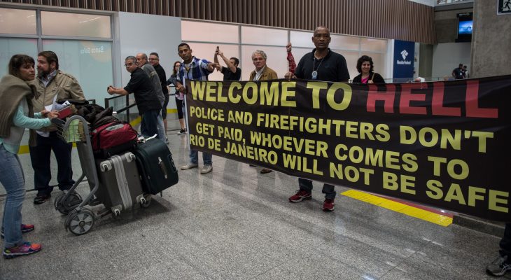 Police officers and firemen welcome passengers with a banner reading "Welcome to Hell" and other slogans as they protest against the government for delay in their salary payments at Tom Jobim International Airport in Rio de Janeiro, Brazil, July 4, 2016. The Police has been mounting street protests since last week, saying that they have not been fully paid for months as Rio state's budget hovers on the edge of bankruptcy. Earlier this month, the state authorities in Rio declared "state of public calamity "about a major crisis budget in order to release emergency funds to finance the Olympic Games due to start in August. / AFP / VANDERLEI ALMEIDA        (Photo credit should read VANDERLEI ALMEIDA/AFP/Getty Images)
